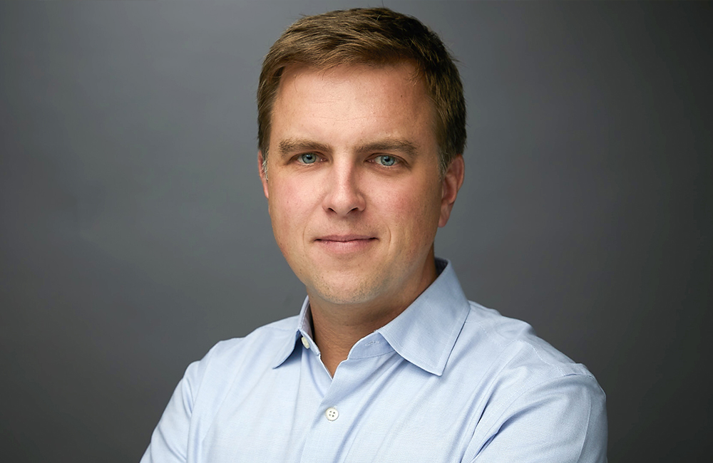 Professional headshot of Alex Hagen in front of a grey background.