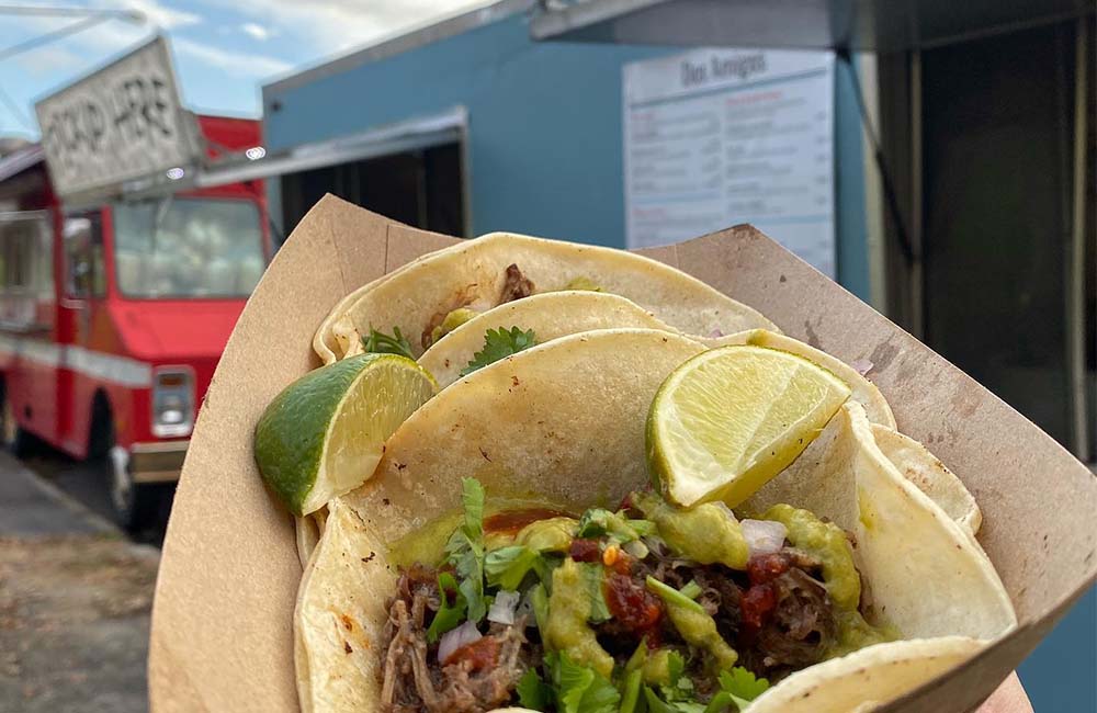 Close-up of a taco in front of the blue Dos Amigos food truck.