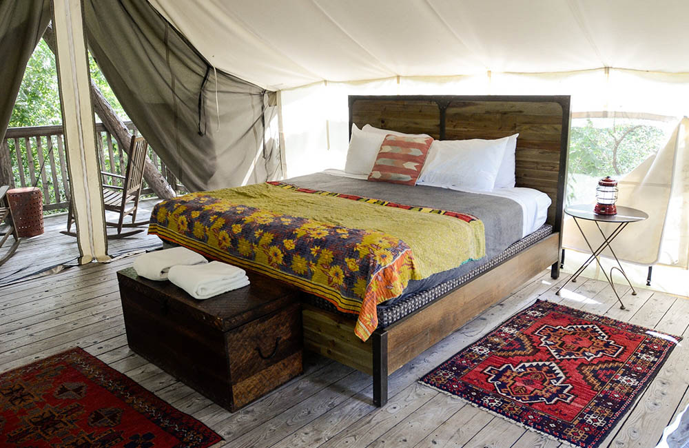 Inside of a tent at Firelight Camps featuring rugs, a luxurious bed, and hardwood floors.