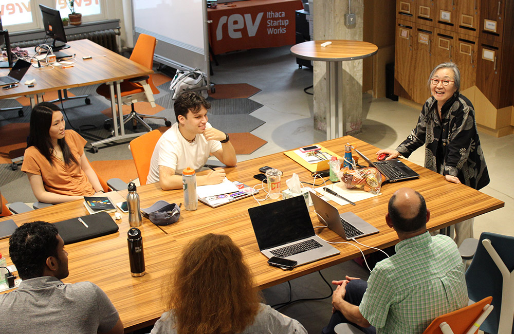 Five participants in Rev's Prototyping and ClimateTech Prototyping programs sit around a table while another person stands and leads a talk.