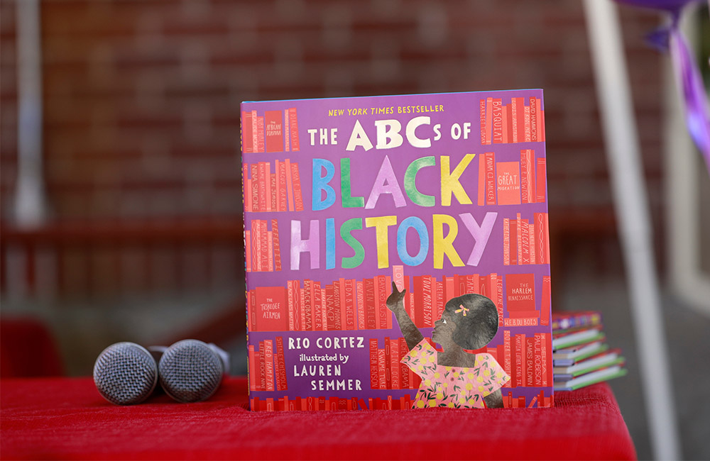 The children's book, "The ABCs of Black History" is displayed next to a microphone on a table covered in a red tablecloth.