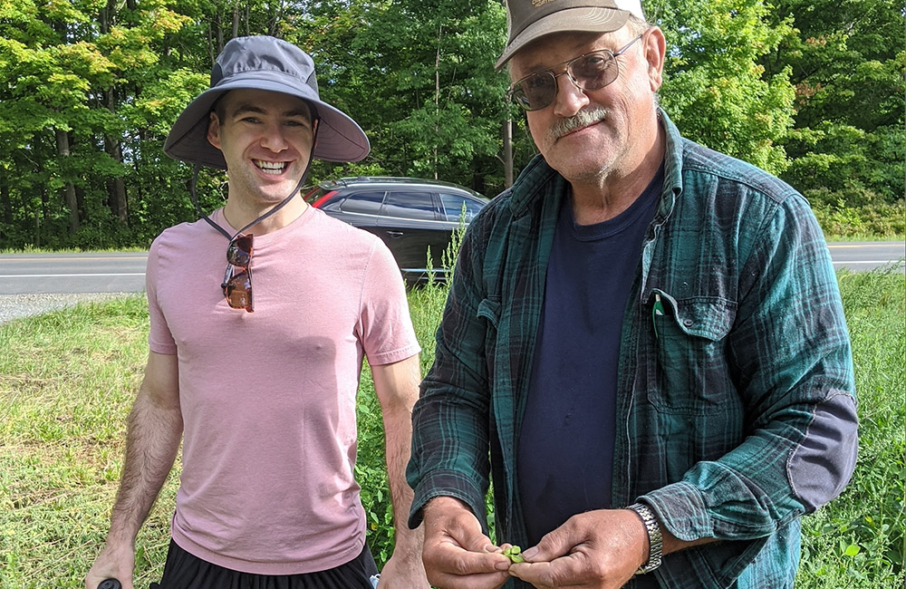 Jason Gooodman, stands next to Carl Taber who is holding green chickpeas in his hands. 