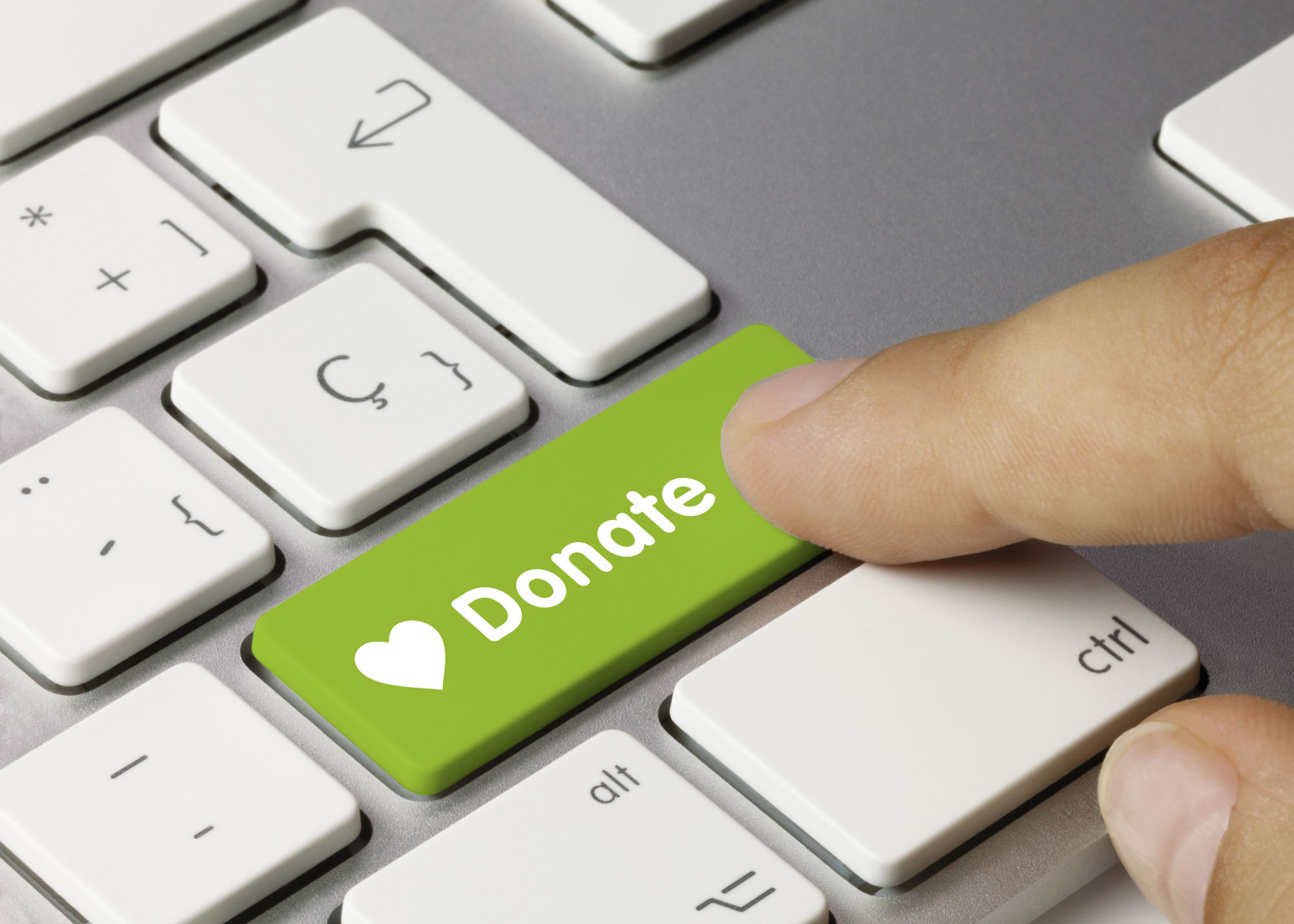 A white and silver computer keyboard has a bright green button with a heart and the word "Donate" which is being pressed by a finger