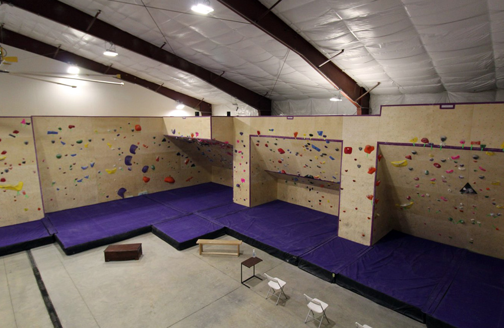 Two large climbing walls at Cayuga Climbs. Purple mats are placed under each climbing wall.