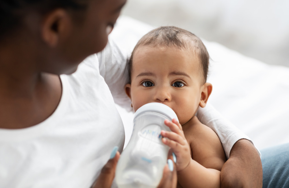 An African American woman cradles her baby while it drinks a bottle.