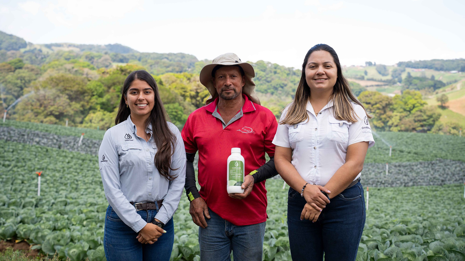 A man holding a bottle of fungicide standing in a field with two women next to him.